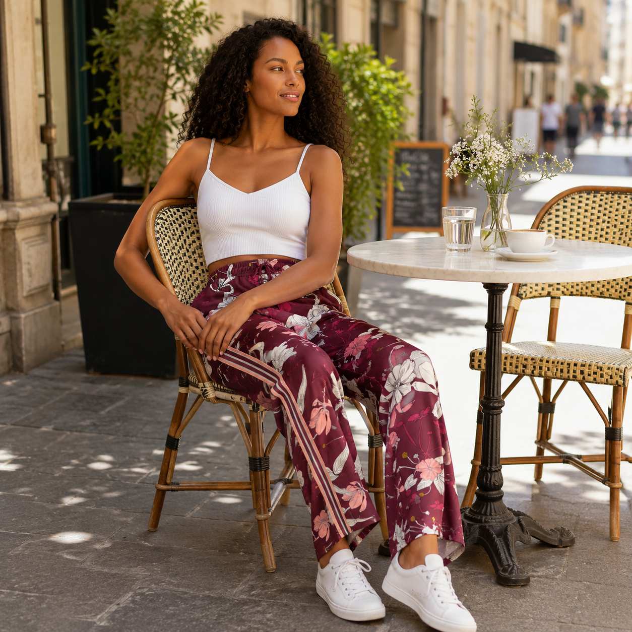 Femme assise en terrasse avec pantalon fleuri bordeaux et baskets blanches